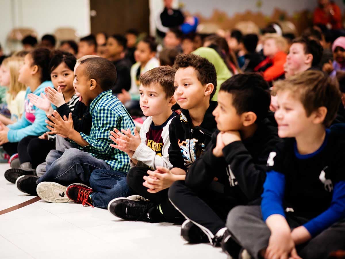 A classroom of children applauds after a performance.