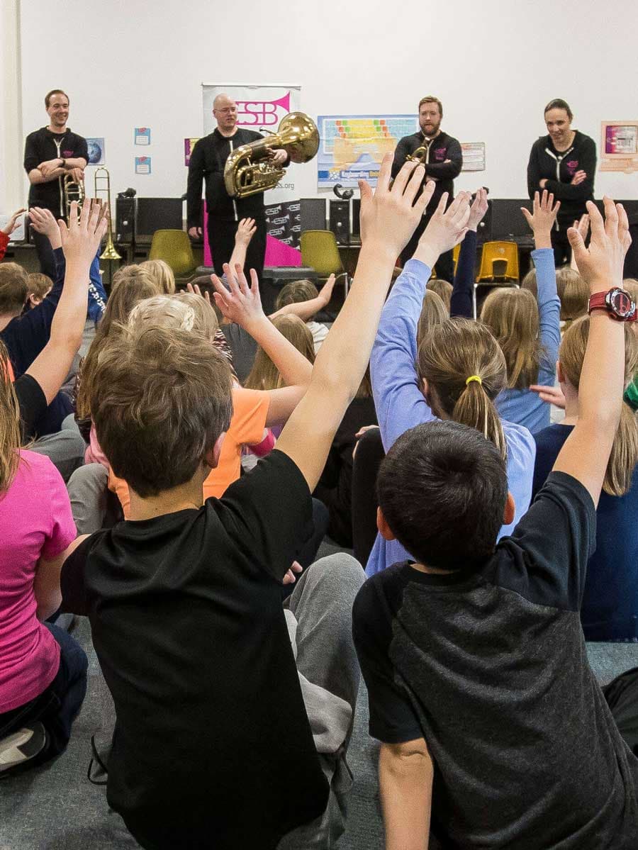 Children raise their hands while watching a brass ensemble.